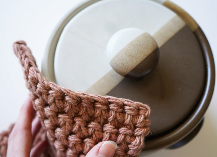 Woven cotton potholder resting on ceramic plate with leather hanger detail — minimalist kitchen essential for heat protection and modern rustic decor.