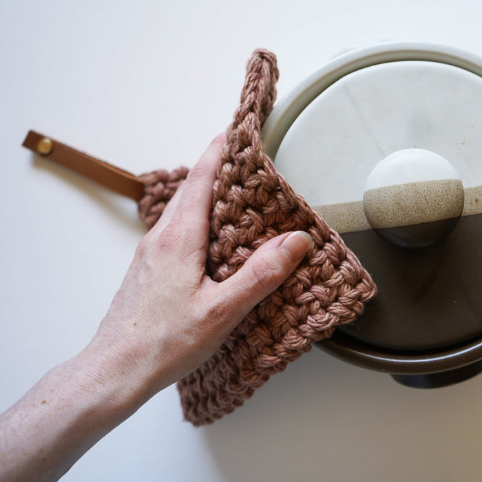 Handwoven cotton potholder with leather strap hanger lifting glass pot lid — thick textured kitchen hot pad designed for heat protection and modern farmhouse cooking.