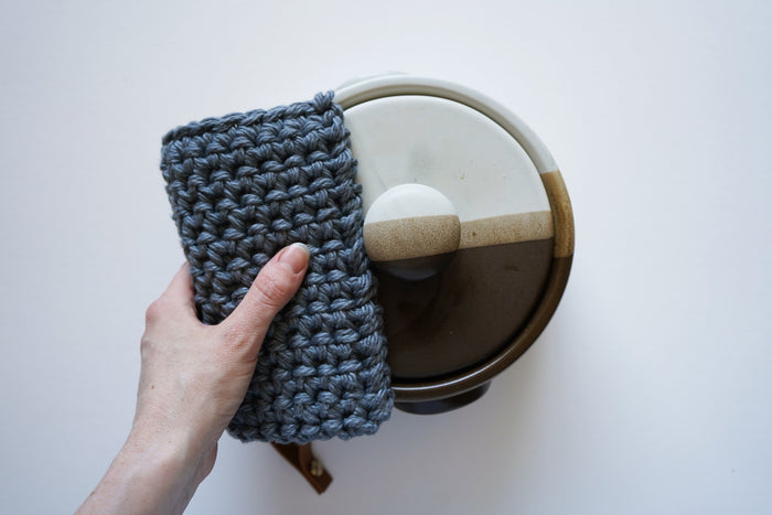 Woven potholder lifting glass lid — heat-protective cotton hot pad with modern leather hanging strap.