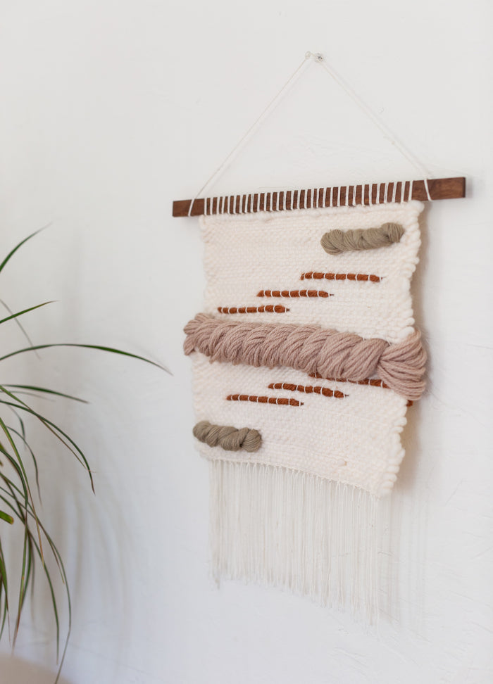 Angled view of contemporary woven wall hanging with braided wool and wood dowel — organic modern textile art.