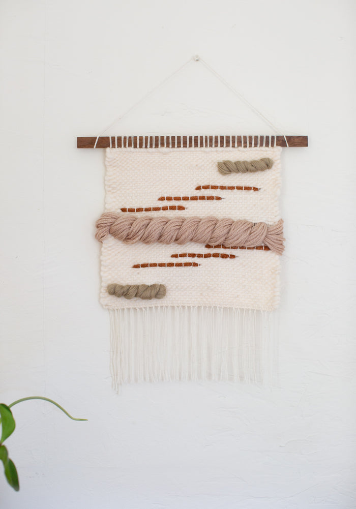 Neutral boho wall hanging with layered wool textures and fringe — simple modern fiber decor for warm interiors.