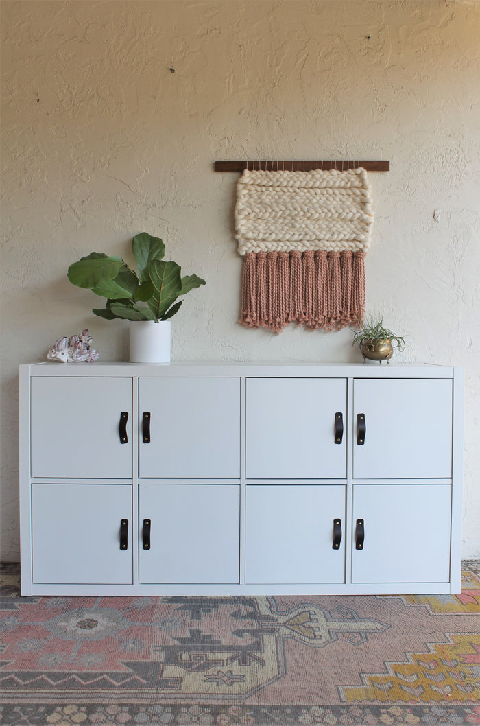 Keyaiira woven wall art displayed above a white cabinet with plant styling, showcasing neutral cream wool, warm mauve fringe, and modern organic home decor