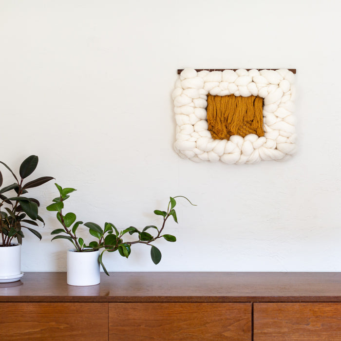 Sesame Cloud textile wall art featuring sculptural cream wool border with mustard fiber center — modern Scandinavian-inspired wall decor styled above wood console.