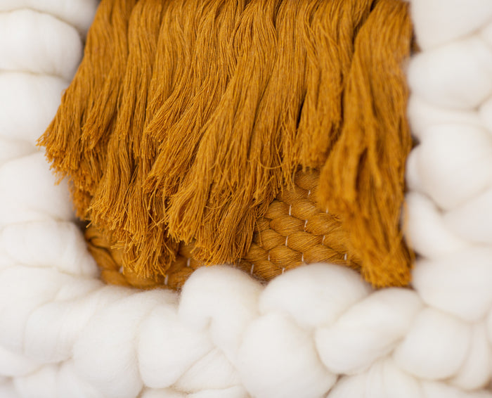 Close-up of Sesame Cloud showing textured mustard yarn center framed by chunky cream wool — dimensional textile wall art detail.