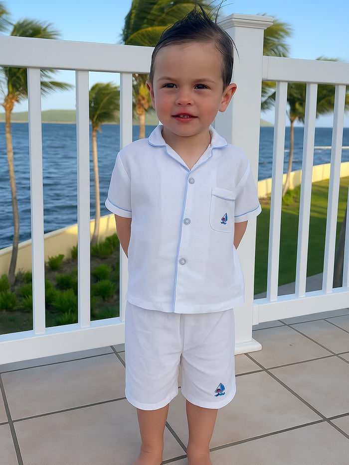 Child in a white outfit standing on a balcony with a scenic view of water and palm trees.