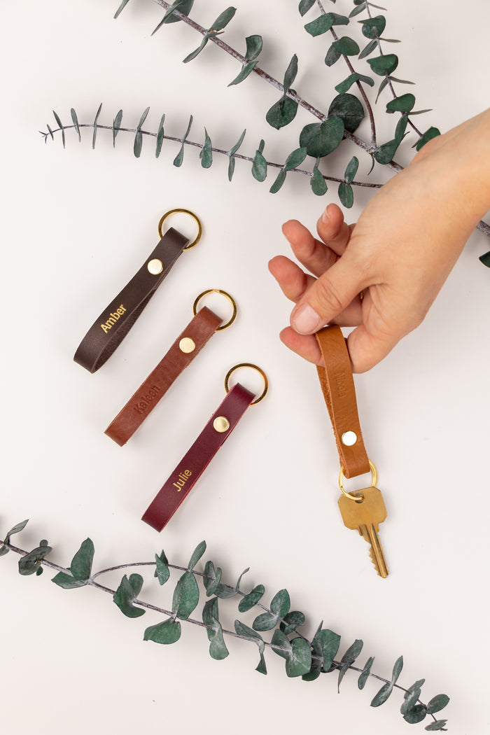 Hand selecting leather loop keychain color options — minimalist key holder with secure snap closure and brass ring.