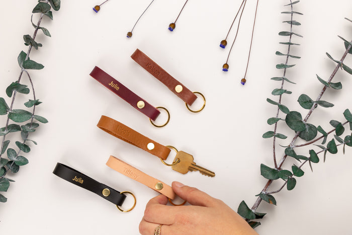 Close-up of engraved skinny leather keychain with brass snap and ring — handcrafted minimalist key accessory.