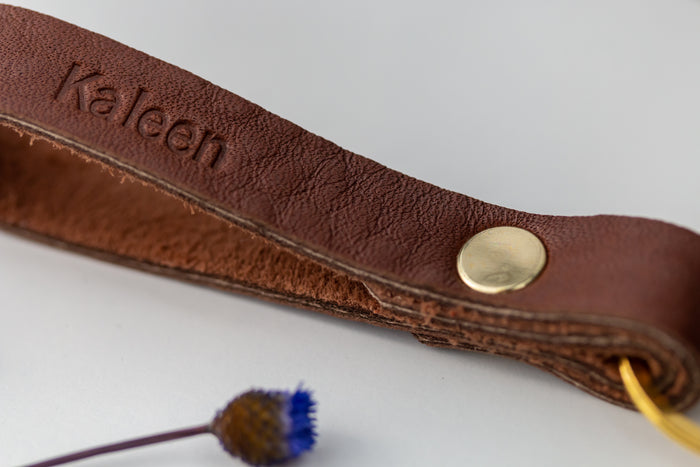 Close-up of engraved skinny leather keychain with brass snap and ring — handcrafted minimalist key accessory.
