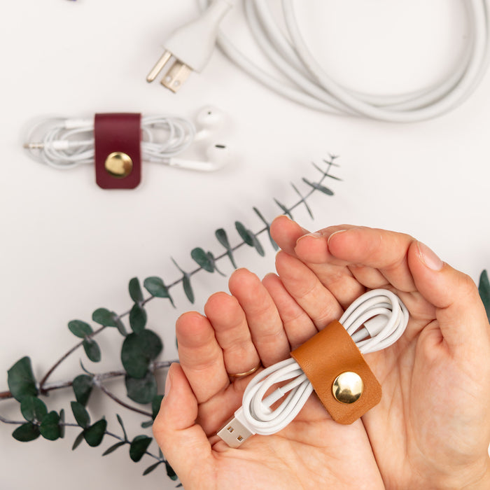 Individually crafted leather cord holder shown organizing a coiled white cable, reusable Keyaiira cable keeper for earbuds, device cords, charger storage and compact tech organization