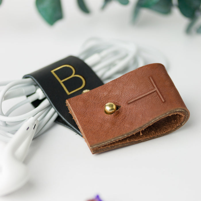 Initialed leather cable holders in Black and rich brown tones, handmade Keyaiira accessories for keeping charging cords, earbuds, USB cables and compact electronics neatly contained