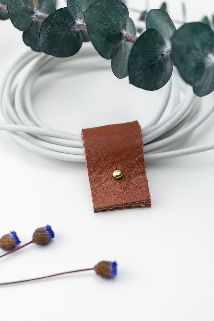 Rich brown full-grain leather charger keeper fitted around a coiled white cable, thoughtfully designed by Keyaiira for compact cord control, device storage and clutter-free organization