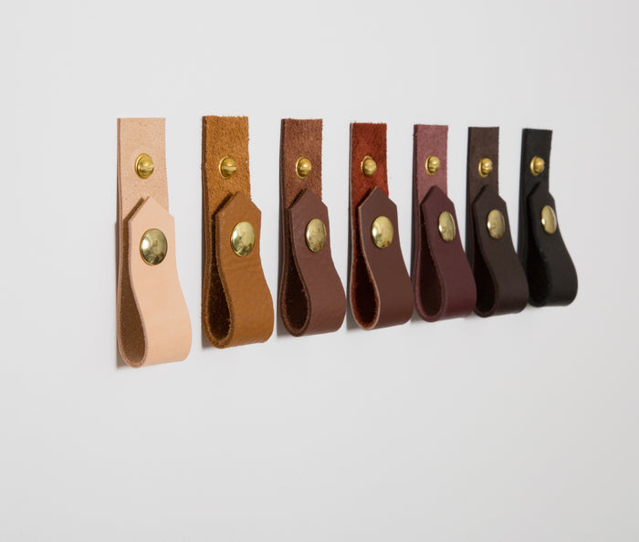 Keyaiira leather wall straps displayed in multiple colorways including natural, cognac, burgundy, black, and brown — handcrafted leather wall hooks with brass hardware.
