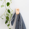 Keyaiira Small Wide Leather Wall Strap in natural veg-tan holding a blue linen towel  minimalist handcrafted leather wall hook with brass hardware for functional home organization.