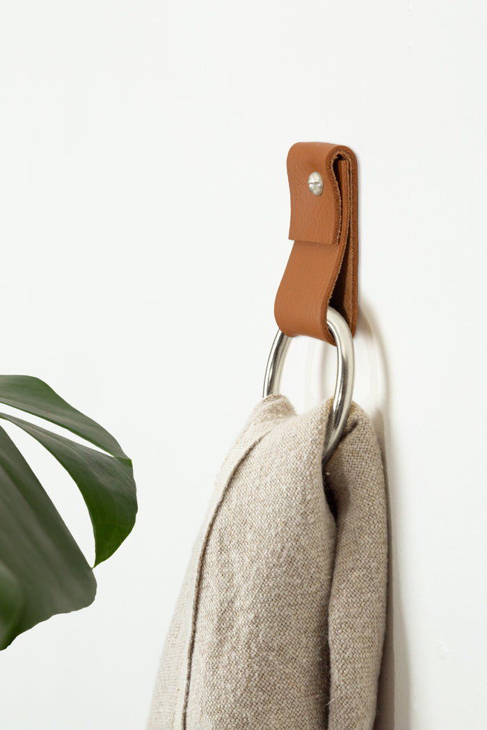 Small Wide Leather Wall Strap in warm cognac brown with silver ring — handcrafted leather towel holder shown with neutral linen towel. Minimal modern wall hardware for bathrooms and kitchens by Keyaiira.