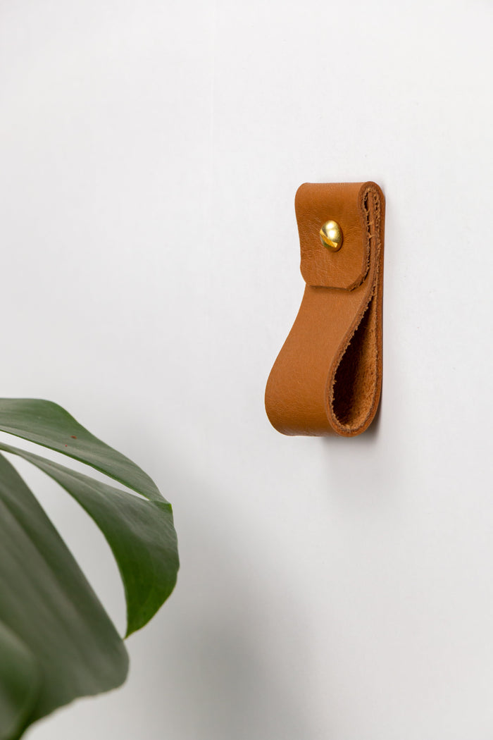 Keyaiira genuine leather wall hanging strap in warm cognac with solid brass rivet, wall-mounted for modern entryway, kitchen, or bathroom organization — minimalist leather wall hook alternative.