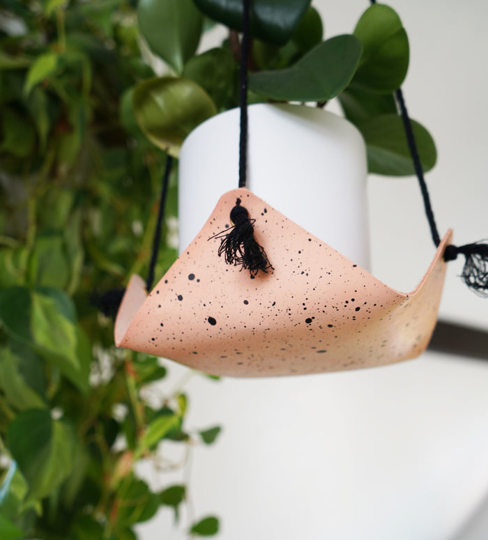Keyaiira speckled leather hanging planter in natural finish with black cord supporting white pot and trailing plant. Handcrafted leather home decor accent for modern plant styling.