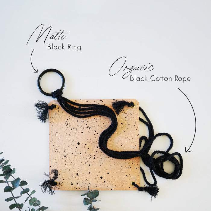 Keyaiira hanging planter components shown flat: speckled leather base paired with matte black metal ring and organic black cotton rope. Handcrafted detail of modern speckled leather plant hanger materials.
