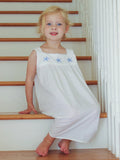Young girl in a white dress with star designs sitting on wooden stairs.