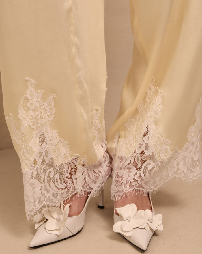 A detailed close-up of the trousers' hem, focusing on the lace accents that soften the silhouette without excess.