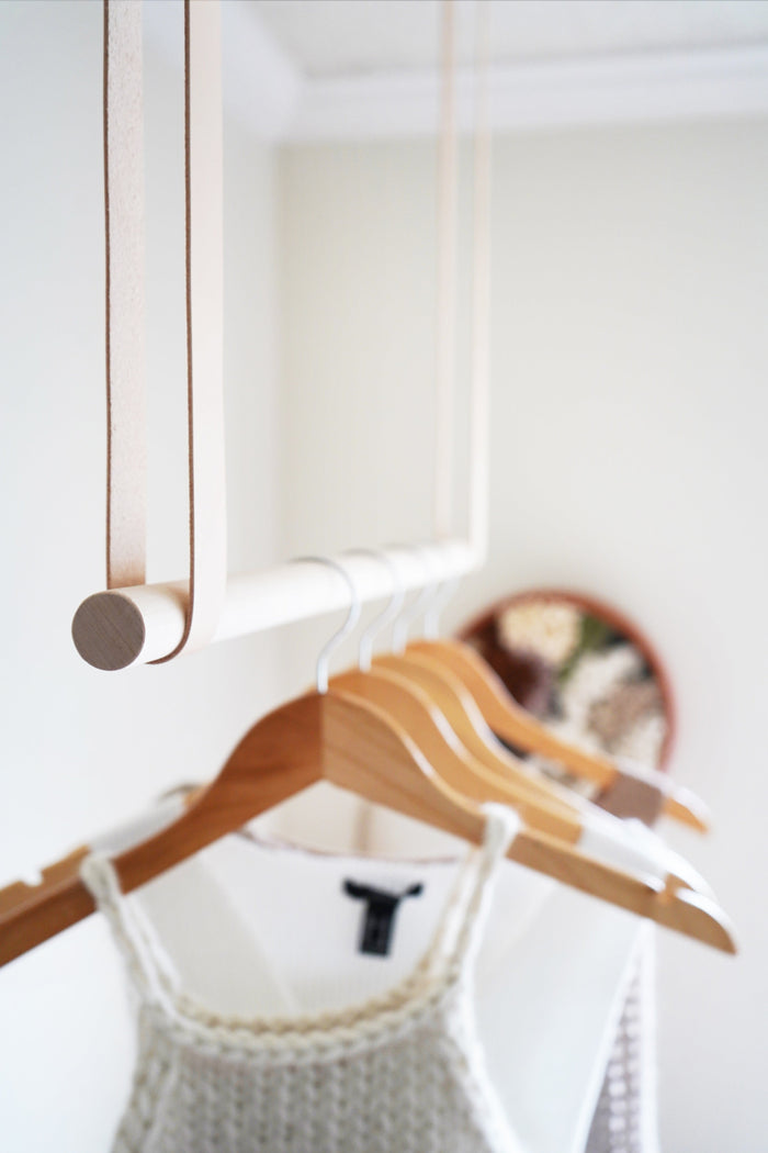 Close-up of Keyaiira hanging rail detail showing handcrafted vegetable-tanned leather straps and light birch wood rod used as a minimalist hanging solution.