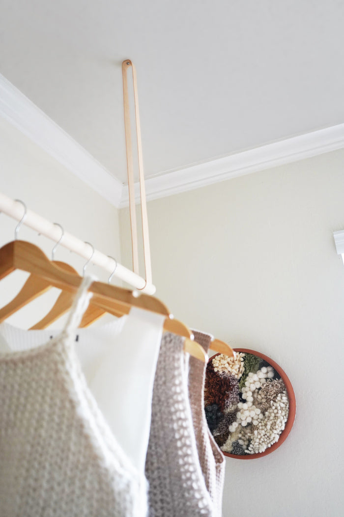 Keyaiira ceiling-mounted garment rack with natural leather straps and birch wood dowel handcrafted hanging clothing rack for minimalist bedroom organization.