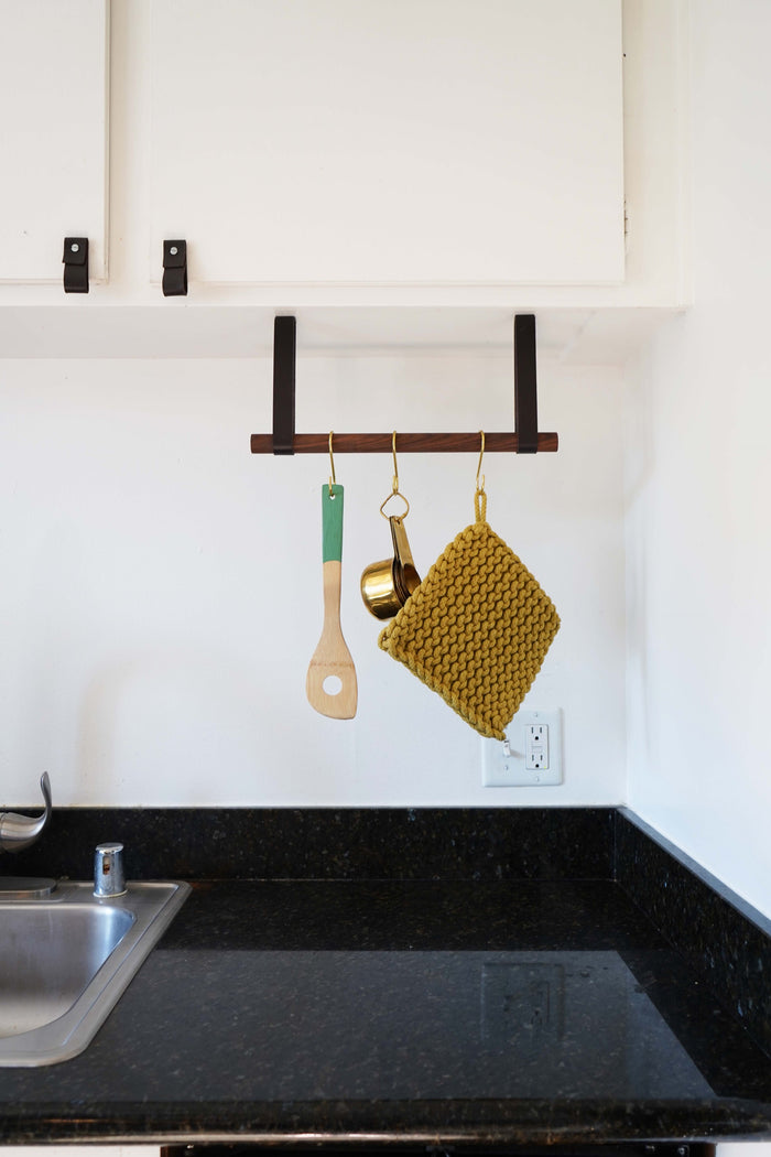 Wall-mounted hanging rail above cooktop — leather strap suspended storage for kitchen utensils and potholders.