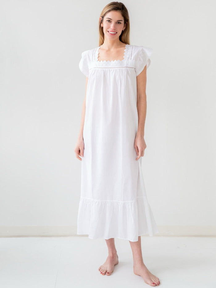A woman standing in a white Genevieve white cotton nightgown with butterfly cap sleeves and a scalloped square neckline.