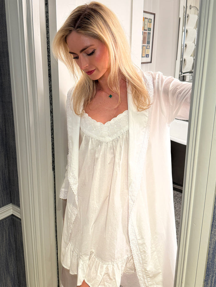 Woman wearing a white lace nightgown with a sheer white cardigan in front of a mirror.