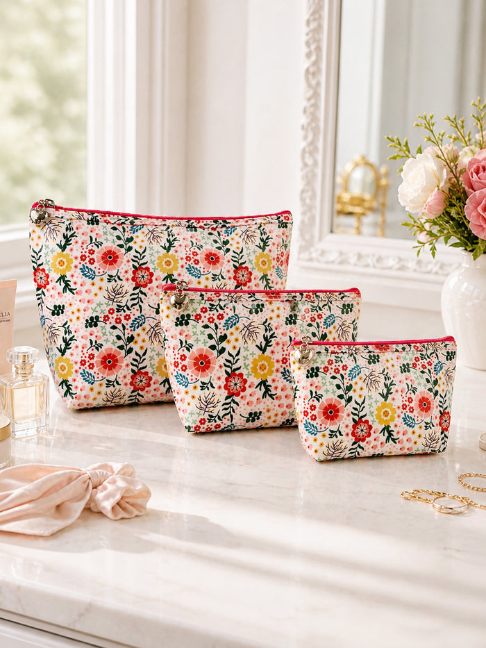 Set of floral-patterned makeup bags on a vanity table with a mirror and flowers in the background.