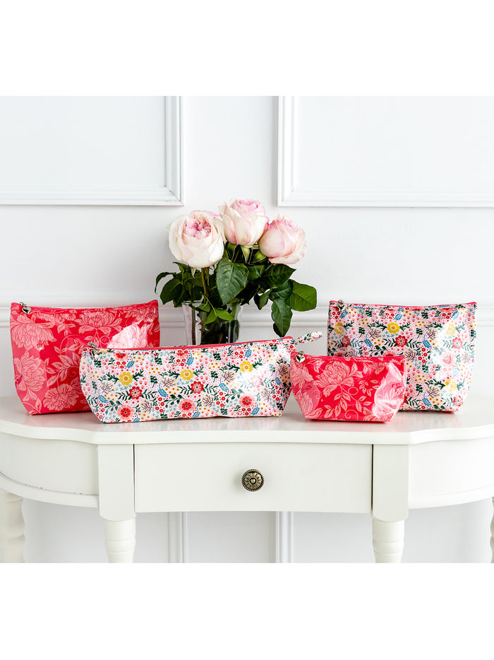 Floral-patterned makeup bags on a white surface with a vase of flowers.