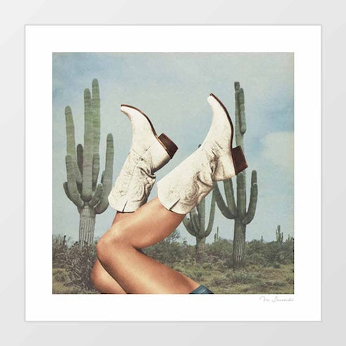 These Boots Cactus Yeehaw art print — bare tanned legs kicked up wearing cream white tooled leather cowboy boots with dark brown contrast heel and intricate embossed scroll detailing against a backdrop of towering Saguaro cacti and a pale bleached blue Arizona desert sky, vintage analogue film aesthetic Southwest cowgirl freedom art print for desert interiors Airbnb spaces and Western boutiques
