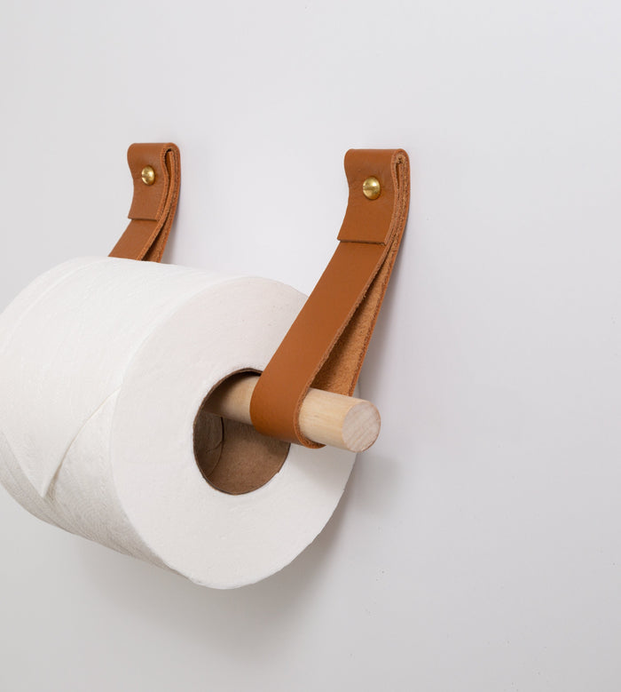 Handcrafted leather strap toilet paper holder with wooden dowel shown in a modern bathroom by Keyaiira.