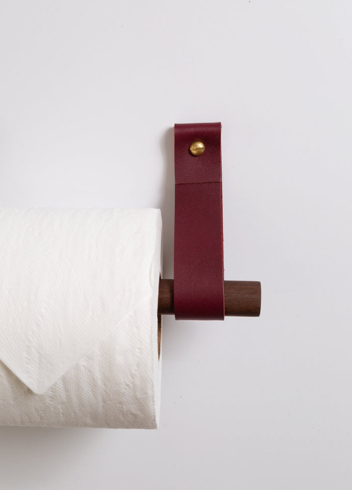 Wine leather toilet paper holder with brass hardware and walnut dowel, handcrafted minimalist bathroom accessory adding rich modern color to your space.