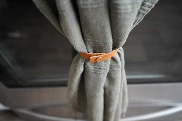 Keyaiira Towel Hugger leather loop in Nicotine shown securing a green kitchen towel on a stainless steel oven handle. Handcrafted vegetable-tanned leather with brass hardware for modern farmhouse kitchen styling.
