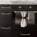 Keyaiira Wide Towel Hugger in warm cognac leather installed on brass oven handle, securing kitchen towel with solid brass hardware — modern farmhouse leather kitchen organizer.
