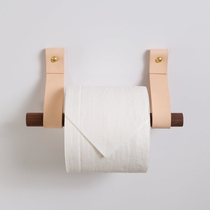 Natural vegetable-tanned leather toilet paper holder by Keyaiira styled with a simple white wall backdrop. Minimal modern bathroom accessory handcrafted from genuine leather and solid brass hardware.