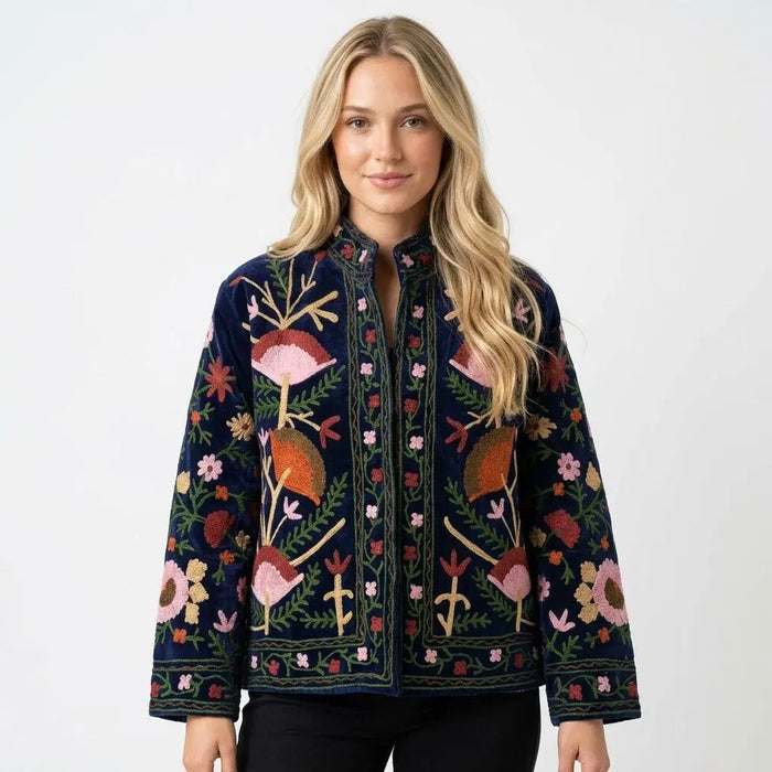 Woman wearing a dark blue embroidered jacket with colorful floral and bird patterns on a white background